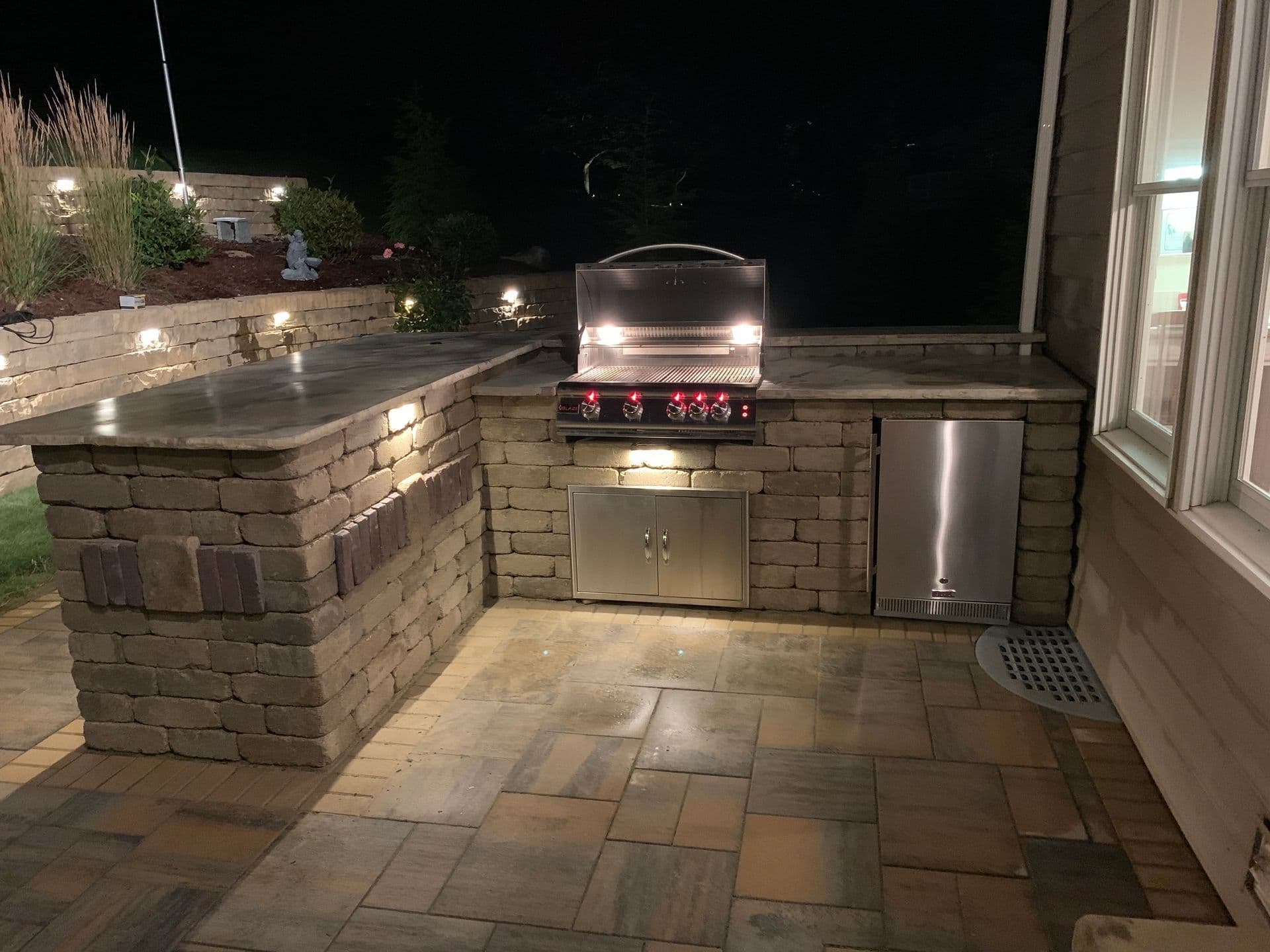 Outdoor kitchen at night featuring a stone grill station with lighting and storage.