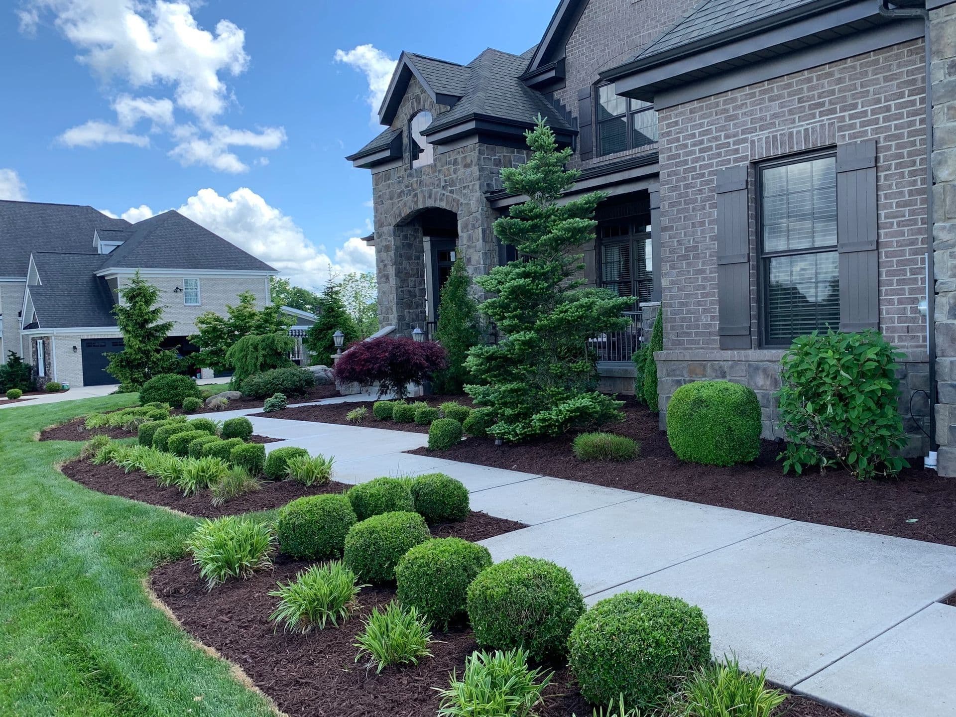 Well-manicured front yard with shrubs, decorative stones, and a modern home in the background.