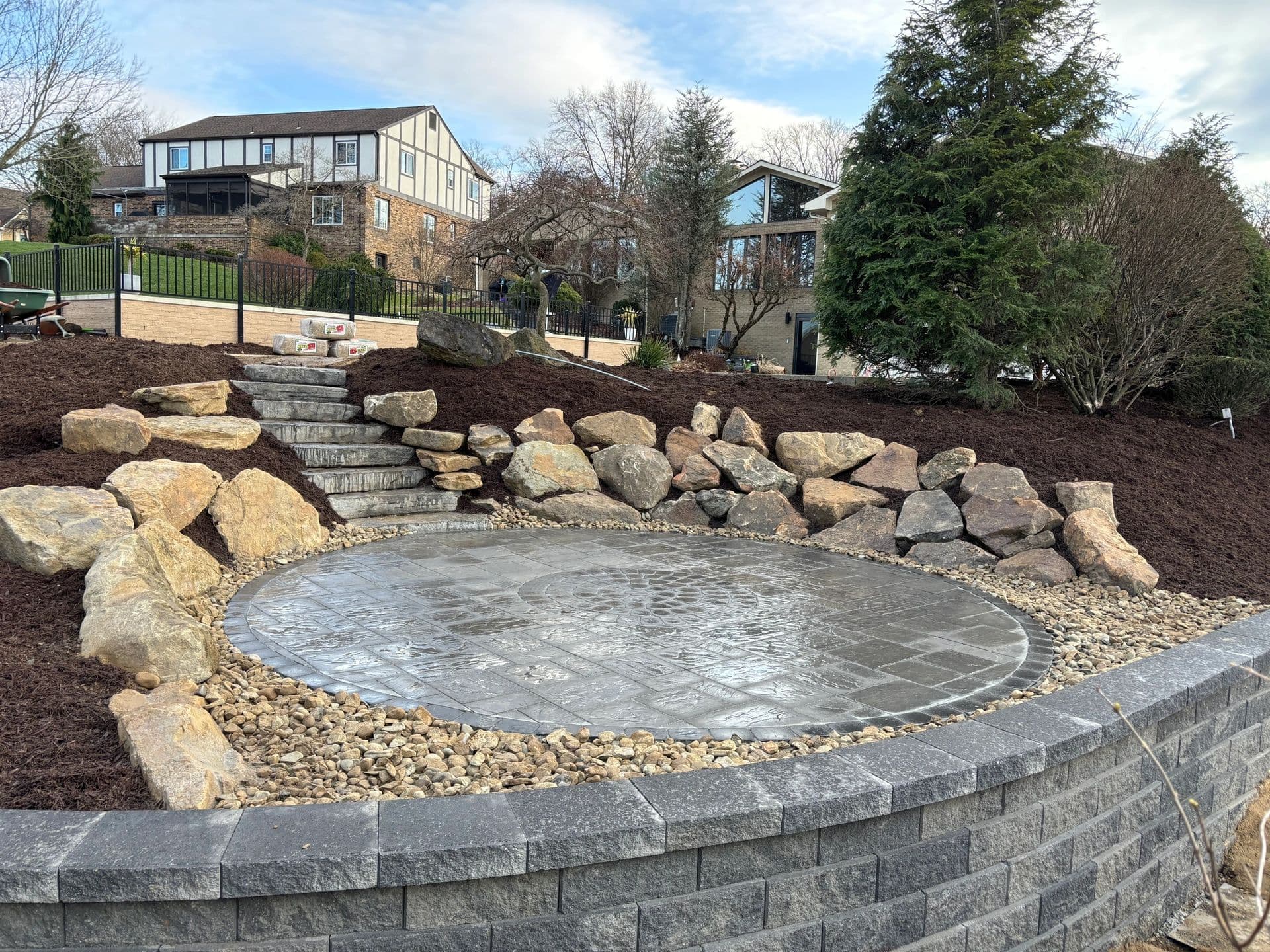 Garden landscaping featuring a stone patio, retaining wall, and decorative boulders.