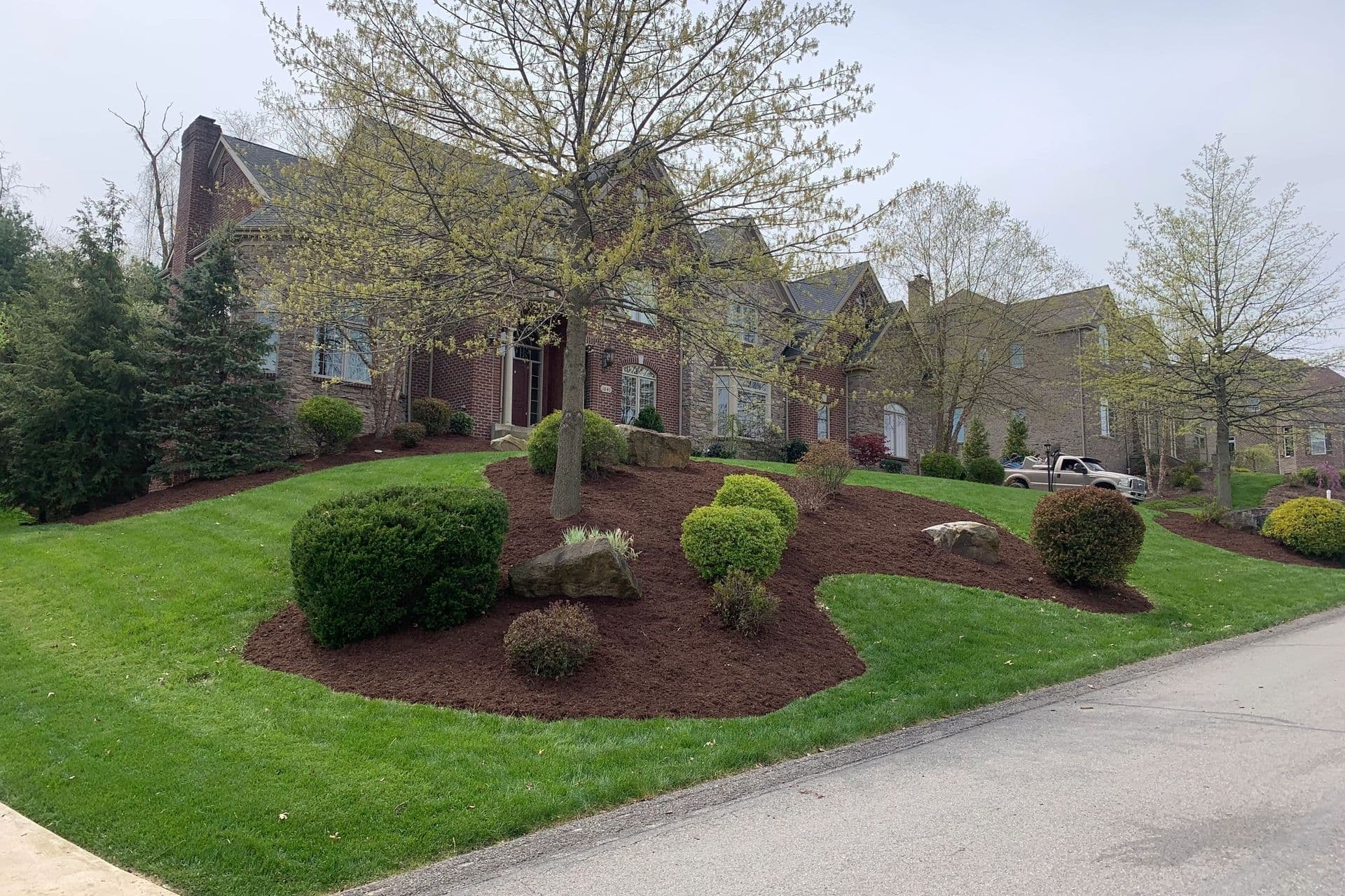 Elegant brick house with landscaped lawn, mulch beds, and green shrubs on a quiet street.